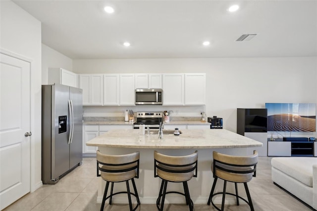 kitchen featuring stainless steel appliances, an island with sink, white cabinets, and a kitchen breakfast bar