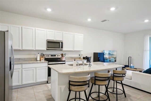 kitchen with stainless steel appliances, an island with sink, white cabinets, and light tile patterned flooring