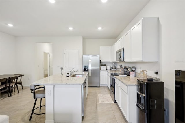 kitchen with sink, appliances with stainless steel finishes, white cabinetry, light stone countertops, and an island with sink