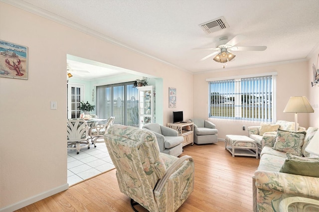 living room featuring plenty of natural light, ornamental molding, ceiling fan, and light wood-type flooring