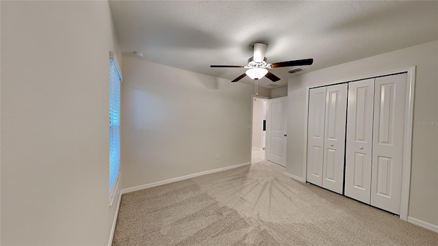 unfurnished bedroom with ceiling fan, a closet, light carpet, and a textured ceiling