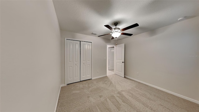 unfurnished bedroom with ceiling fan, light colored carpet, a textured ceiling, and a closet