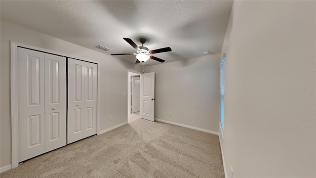 unfurnished bedroom featuring ceiling fan, light carpet, a textured ceiling, and a closet