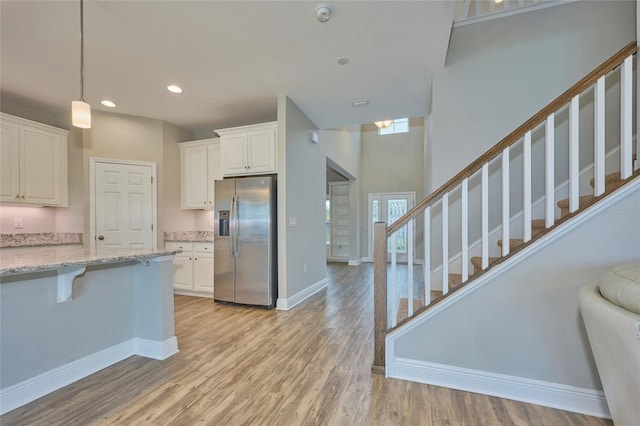 kitchen featuring stainless steel refrigerator with ice dispenser, white cabinetry, pendant lighting, light stone countertops, and light hardwood / wood-style floors