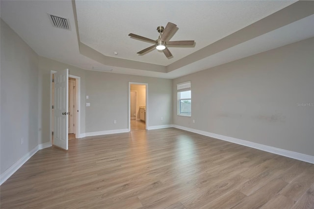 empty room featuring a tray ceiling, light hardwood / wood-style floors, and ceiling fan