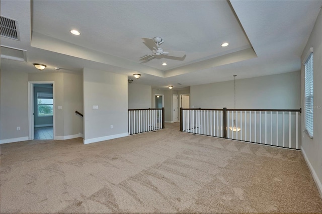 carpeted spare room featuring ceiling fan and a raised ceiling