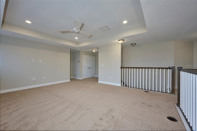 carpeted empty room with a raised ceiling, a textured ceiling, and ceiling fan