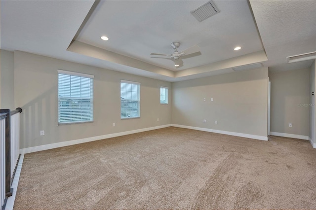 spare room with a raised ceiling, light carpet, and ceiling fan