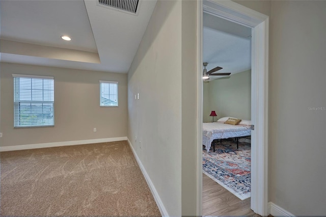 hallway featuring light carpet and a tray ceiling