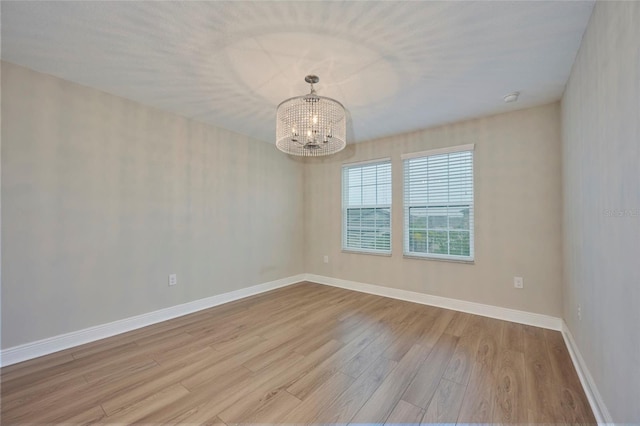 unfurnished room featuring a notable chandelier and light hardwood / wood-style flooring