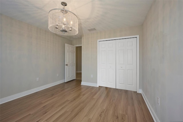 unfurnished bedroom featuring an inviting chandelier, a closet, and hardwood / wood-style flooring