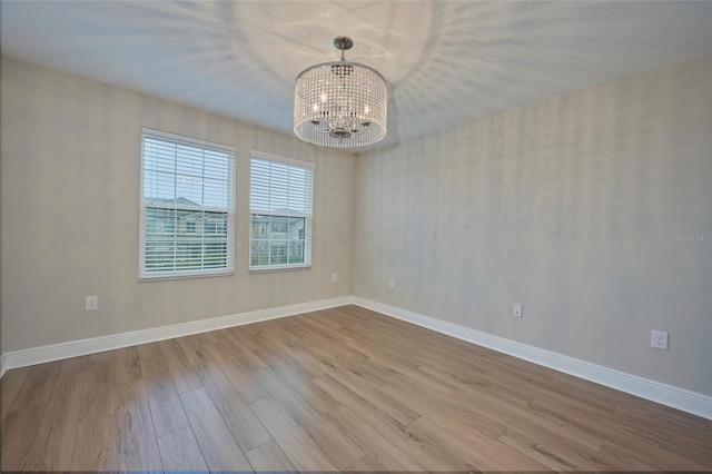 empty room with an inviting chandelier and light hardwood / wood-style flooring