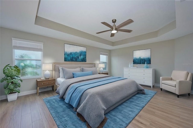 bedroom with multiple windows, a raised ceiling, and light wood-type flooring