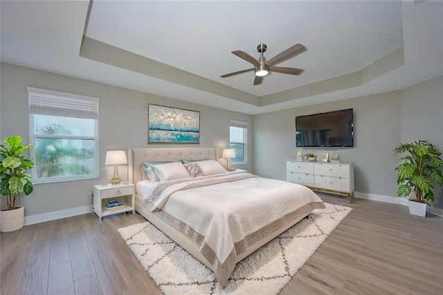 bedroom featuring wood-type flooring, a raised ceiling, and multiple windows