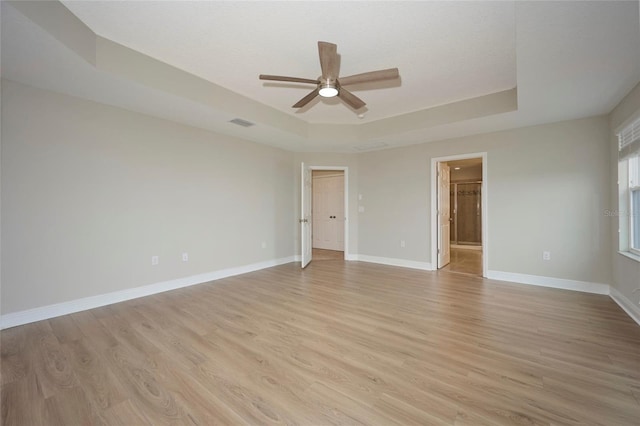 empty room with light hardwood / wood-style flooring, a raised ceiling, and ceiling fan