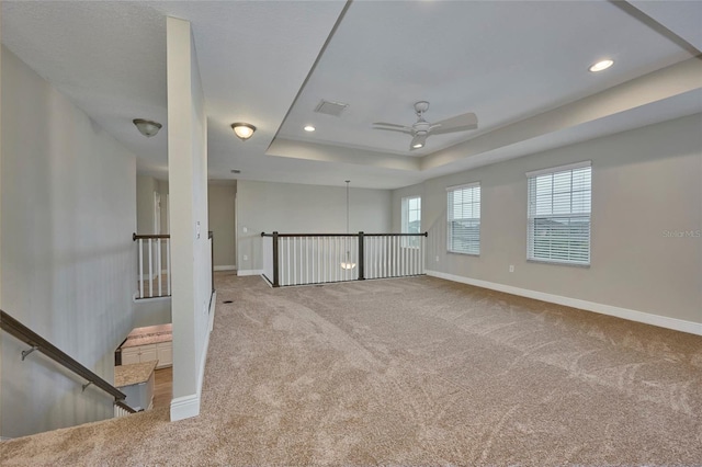 carpeted spare room with a raised ceiling and ceiling fan