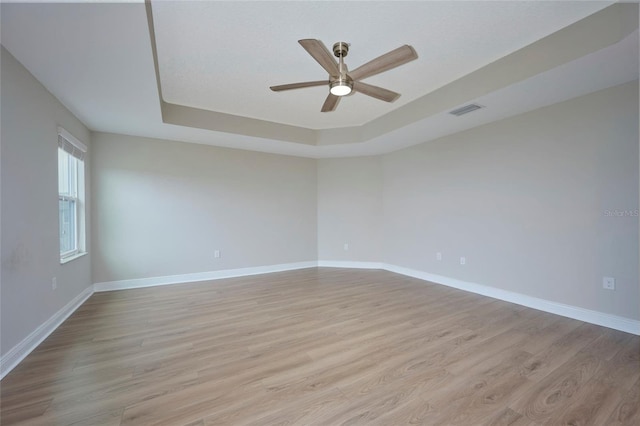 unfurnished room with ceiling fan, a raised ceiling, and light wood-type flooring