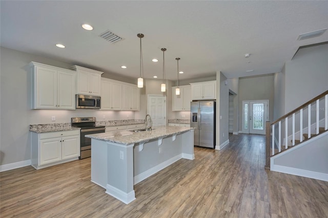 kitchen featuring stainless steel appliances, light stone counters, white cabinets, decorative light fixtures, and sink