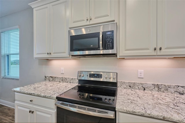 kitchen with white cabinets, appliances with stainless steel finishes, light stone countertops, and dark hardwood / wood-style floors