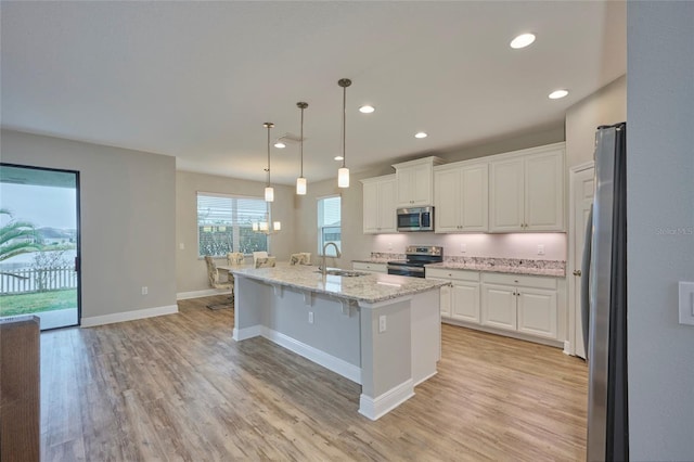 kitchen featuring appliances with stainless steel finishes, a center island with sink, white cabinets, decorative light fixtures, and sink