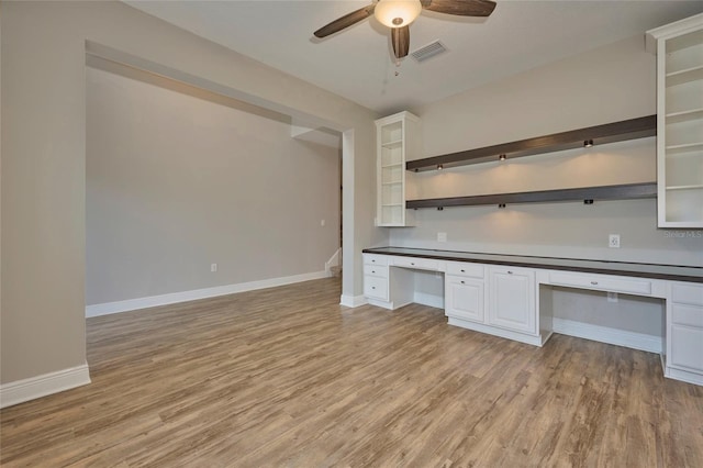 unfurnished office featuring ceiling fan, white cabinets, built in desk, and light hardwood / wood-style floors