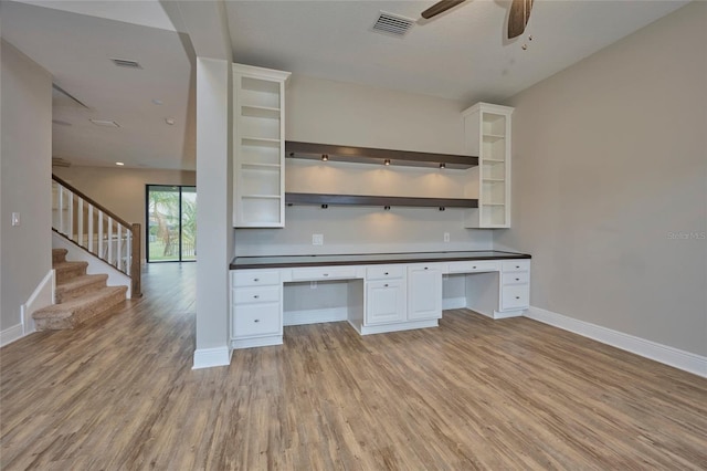 unfurnished office featuring light wood-type flooring, built in desk, and ceiling fan