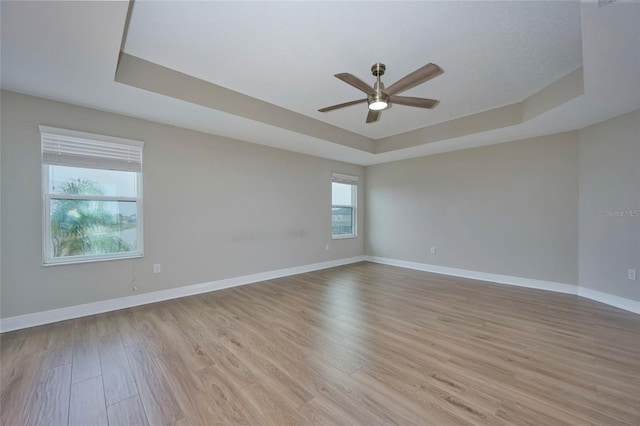 empty room featuring a tray ceiling, ceiling fan, and light hardwood / wood-style flooring