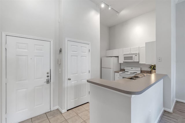 kitchen featuring sink, white appliances, white cabinetry, a high ceiling, and kitchen peninsula