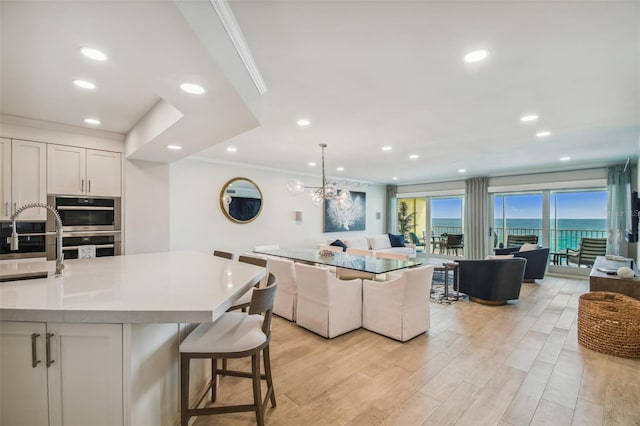 kitchen featuring hanging light fixtures, ornamental molding, light hardwood / wood-style floors, white cabinets, and stainless steel double oven