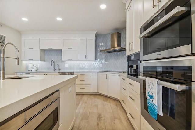 kitchen featuring white cabinets, light wood-type flooring, and wall chimney range hood