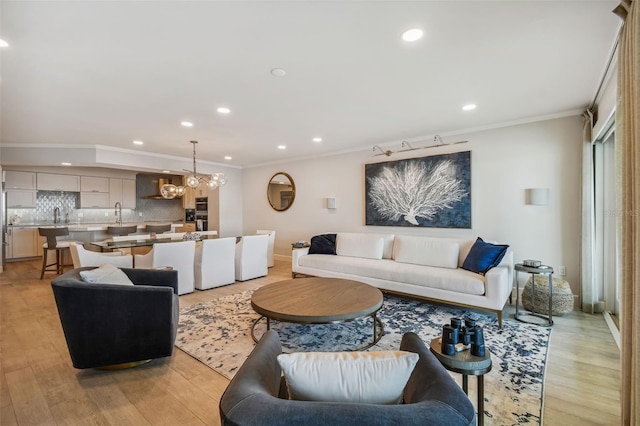 living room with ornamental molding, a chandelier, sink, and light hardwood / wood-style flooring