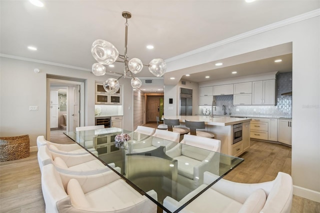 dining room with sink, ornamental molding, and light hardwood / wood-style floors