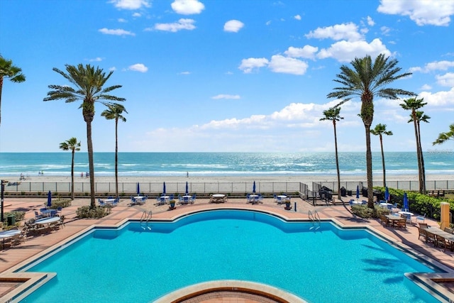 view of swimming pool with a patio, a beach view, and a water view