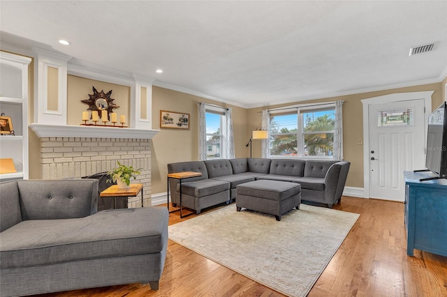 living room with a brick fireplace, ornamental molding, and light hardwood / wood-style floors