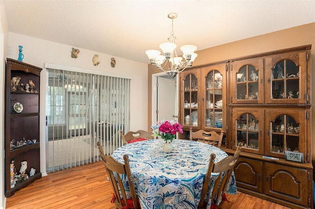 dining room with light wood-type flooring, a textured ceiling, and a notable chandelier