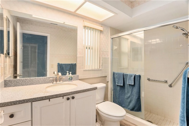 bathroom featuring vanity, toilet, a shower with shower door, and tile walls