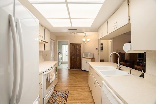 kitchen with washer / clothes dryer, sink, hanging light fixtures, light hardwood / wood-style floors, and white appliances