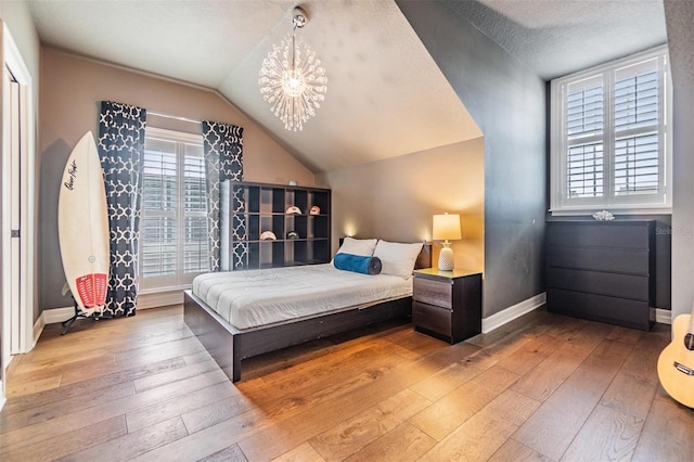 bedroom with hardwood / wood-style floors, a notable chandelier, vaulted ceiling, and a textured ceiling