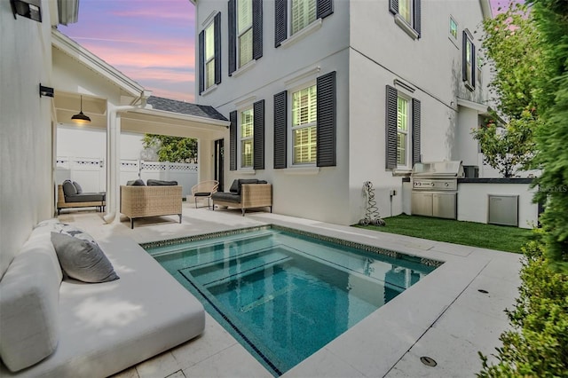 pool at dusk featuring exterior kitchen, area for grilling, and a patio area