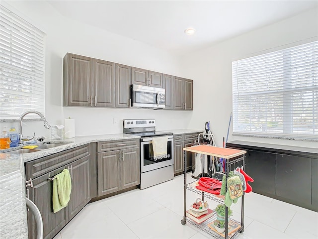 kitchen with light stone countertops, appliances with stainless steel finishes, sink, and light tile patterned floors