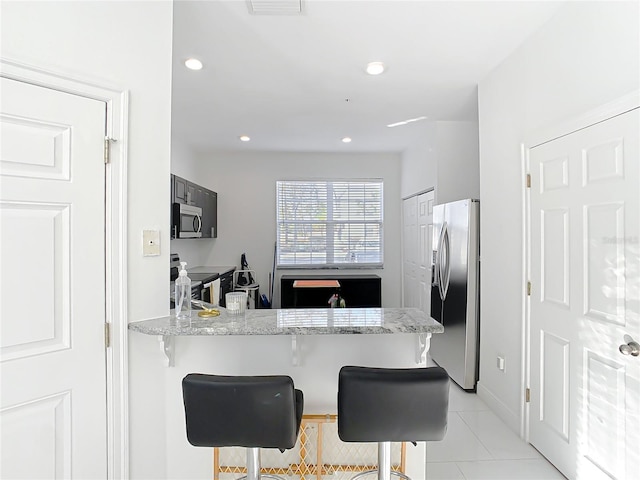 kitchen featuring light tile patterned floors, a breakfast bar area, appliances with stainless steel finishes, light stone counters, and kitchen peninsula