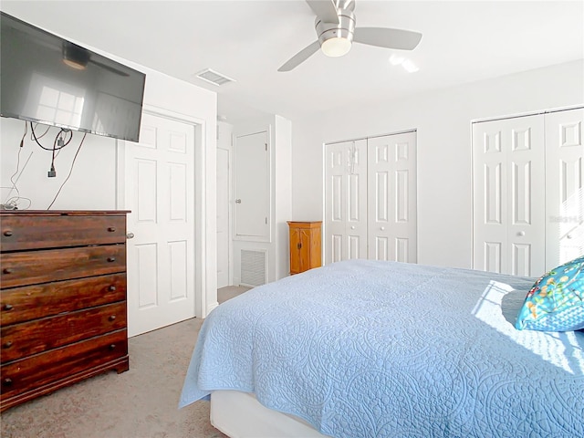 carpeted bedroom with ceiling fan and two closets