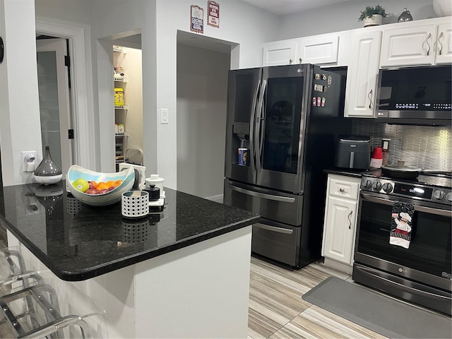 kitchen featuring white cabinetry, appliances with stainless steel finishes, dark stone countertops, and a kitchen breakfast bar