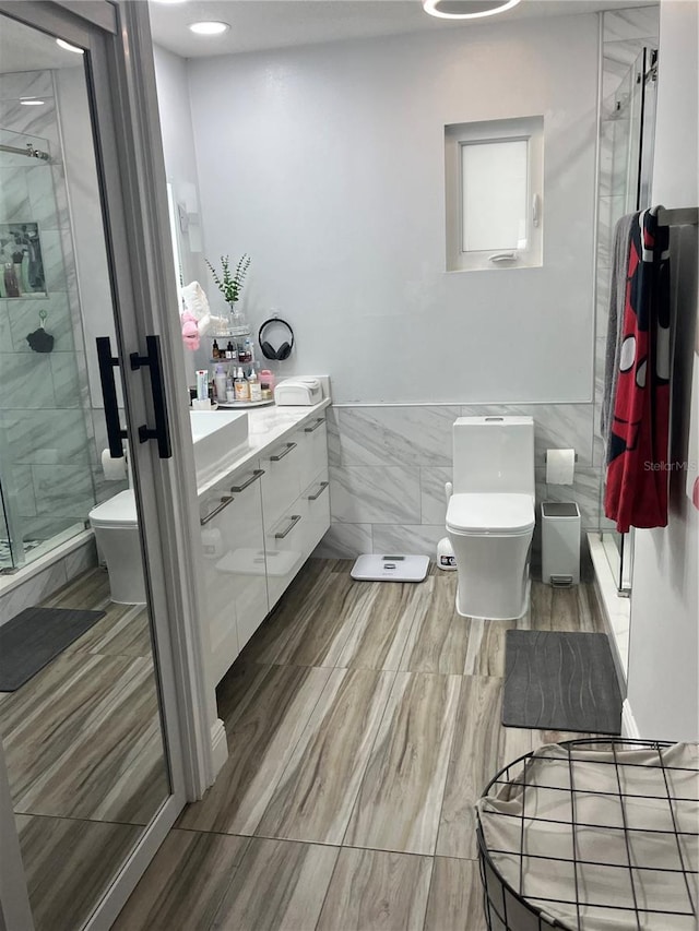 bathroom with vanity, toilet, an enclosed shower, and tile walls