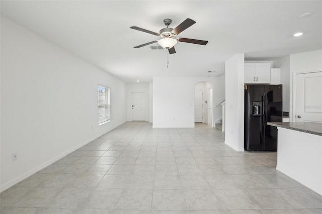 unfurnished living room with arched walkways, light tile patterned flooring, visible vents, baseboards, and a ceiling fan