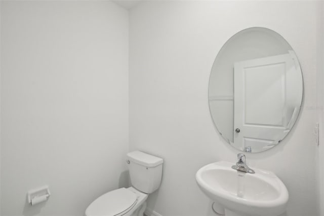 half bathroom featuring toilet, baseboards, and a sink