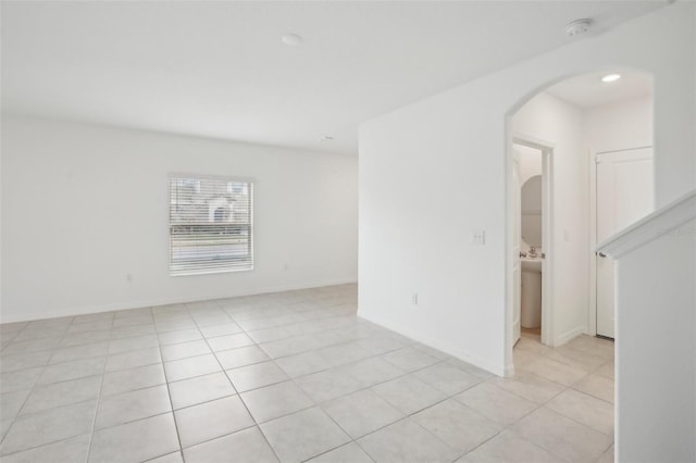 unfurnished room featuring light tile patterned floors, baseboards, and arched walkways