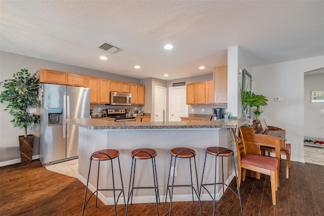 kitchen with appliances with stainless steel finishes, a kitchen breakfast bar, a textured ceiling, kitchen peninsula, and light wood-type flooring