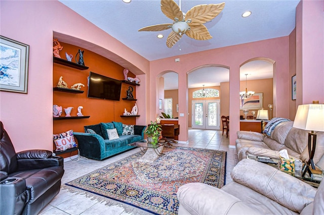 tiled living room featuring ceiling fan with notable chandelier and french doors