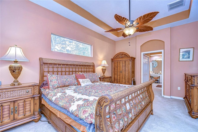 bedroom featuring a tray ceiling, light colored carpet, ceiling fan, and ensuite bathroom